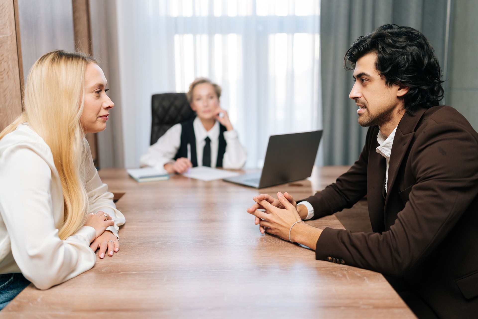 Sad young man and woman looking at each other angrily getting divorced sitting at table with layer in office. Dissolution of marriage of two adults.